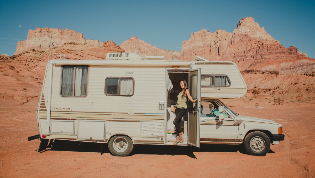 A woman standing in the doorway of her parked RV. She is camping out in a remote desert environment.