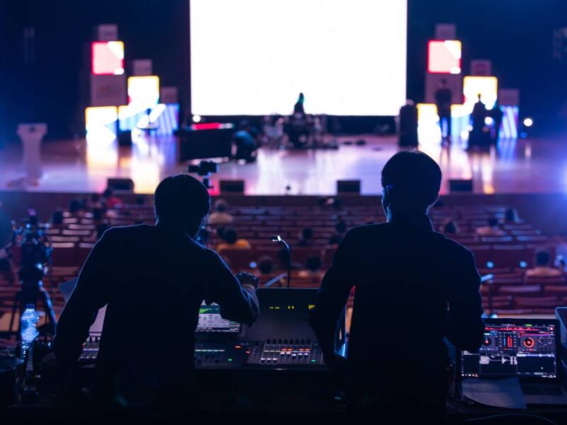 Two event producers are standing at a sound console during sound check while looking out toward the main stage.