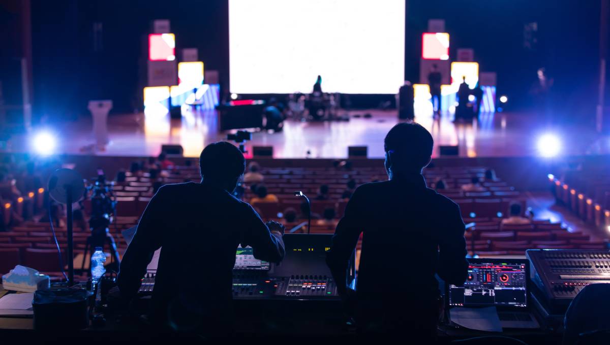 Two event producers are standing at a sound console during sound check while looking out toward the main stage.