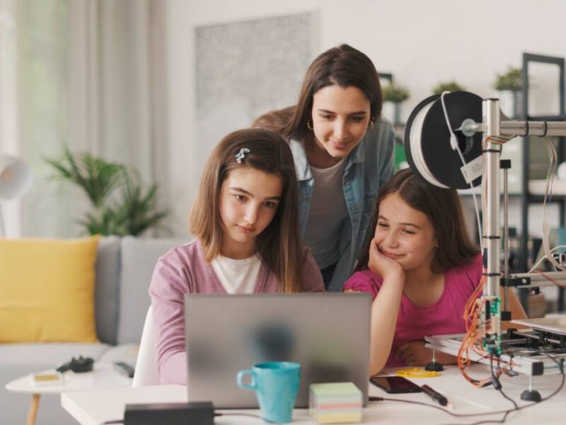 Two girls sitting in front of a computer at home with their mother working on a design for a 3D printer.