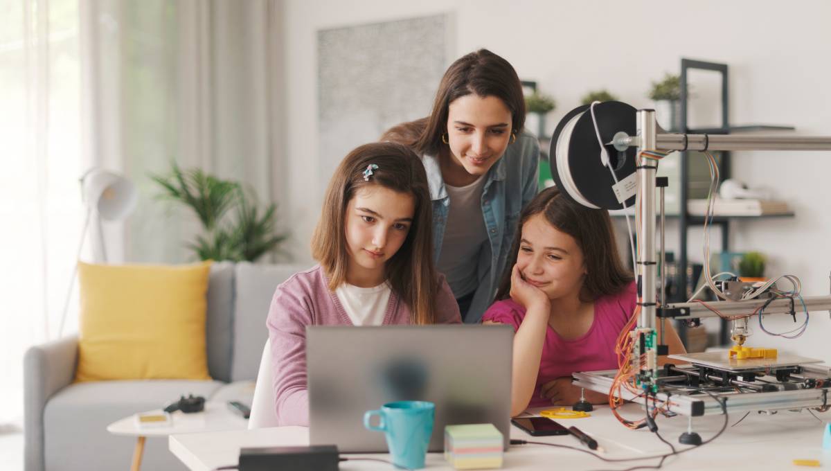Two girls sitting in front of a computer at home with their mother working on a design for a 3D printer.