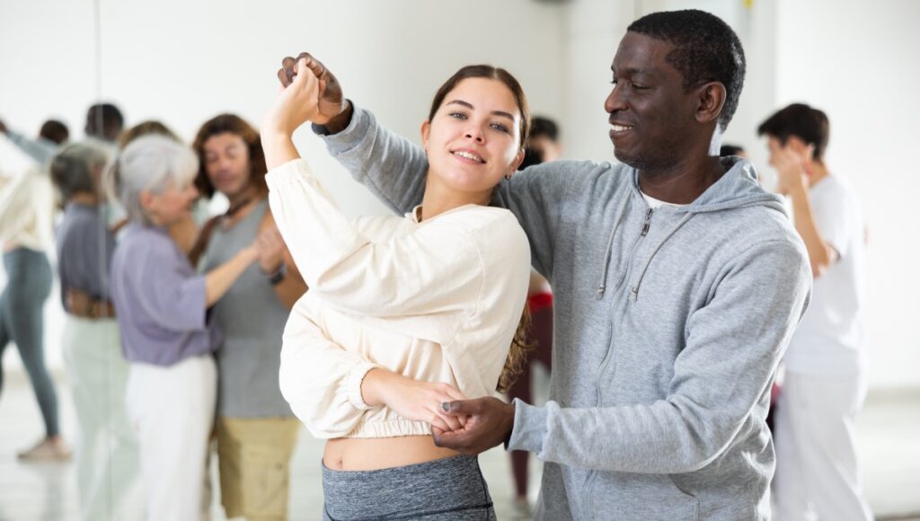 A middle-aged couple practicing a ballroom dance spin. The pair are in a ballroom dance class, enhancing their technique