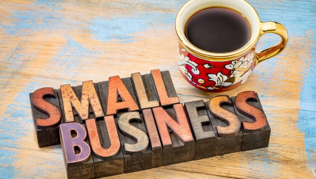 Wood, letterpress-type blocks spell out “small business” next to a red, floral-patterned mug full of coffee.