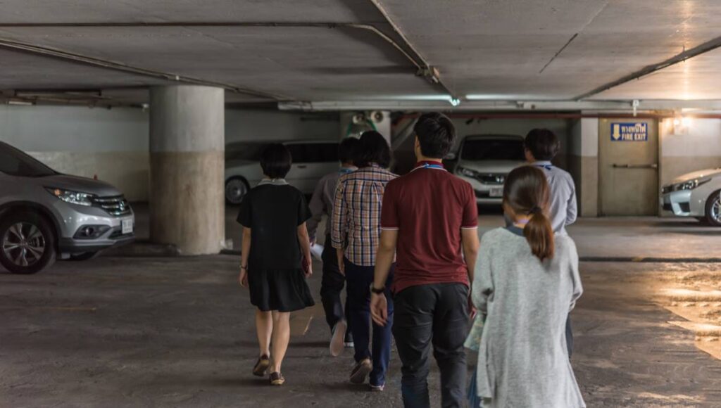 A group of six people wearing lanyards and walking through a parking garage together with their backs to the camera.