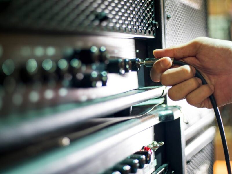 A person’s hand holding a guitar cable while getting ready to plug the jack into the input on a large amplifier.