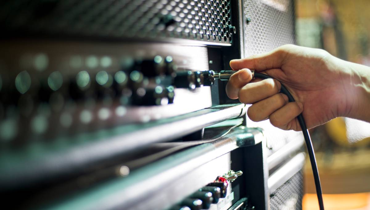 A person’s hand holding a guitar cable while getting ready to plug the jack into the input on a large amplifier.