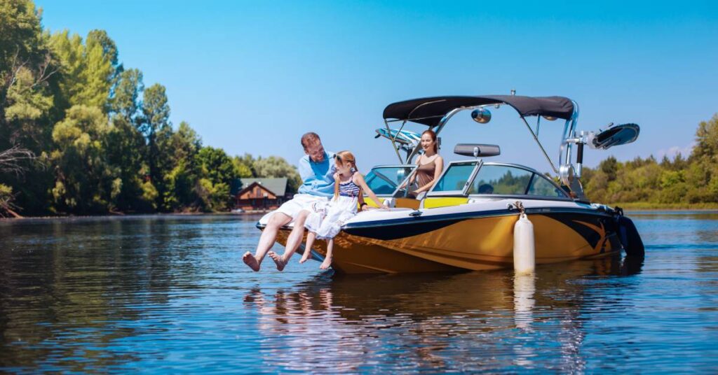 A father and daughter sit on the front part a stopped boat, dangling their feet above the water. A woman stands behind the wheel.