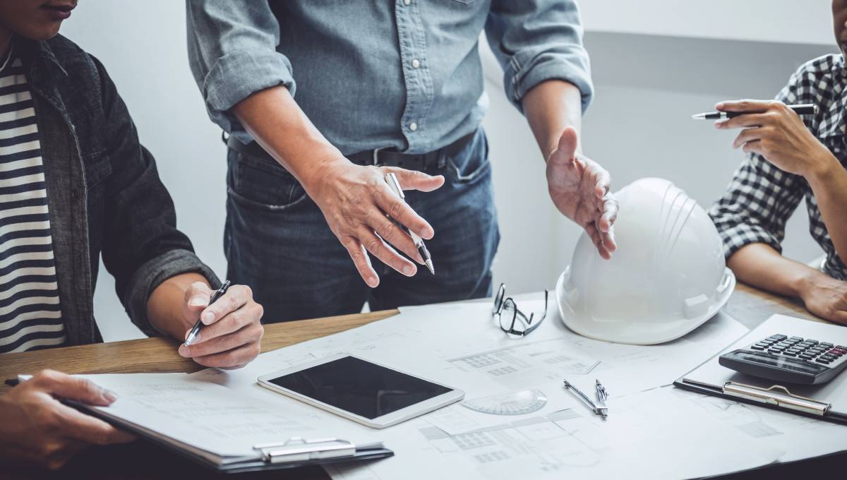 Two engineers discussing project plans and reviewing blueprints on a construction site with safety helmets on a table.