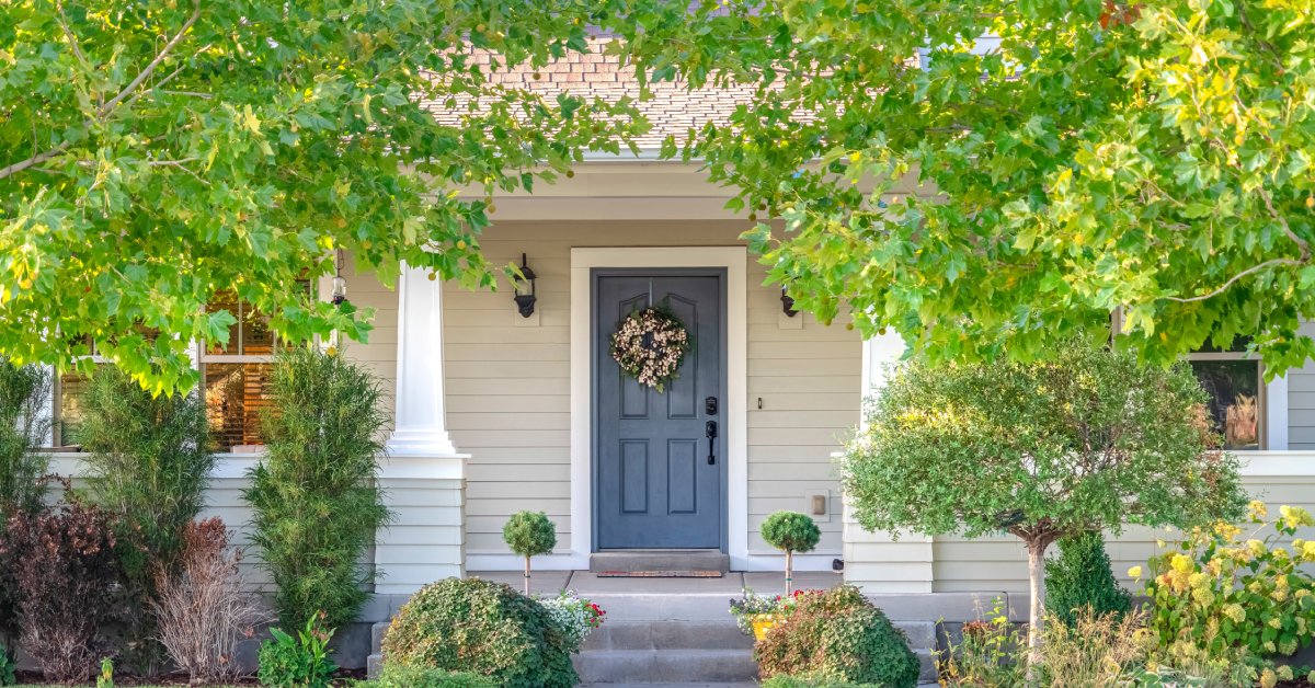 A blue front door with a wreath on it. The door is framed by leaves of trees planted on either side of the house.