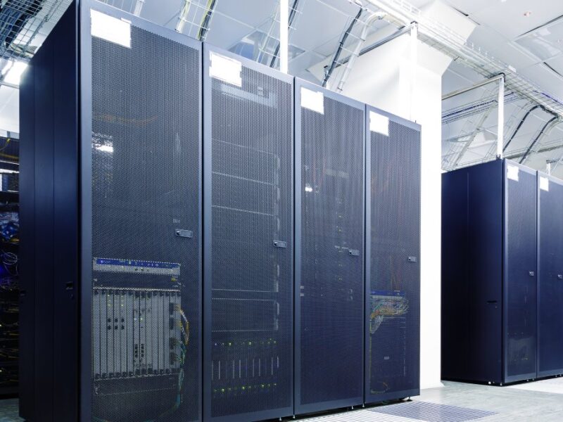 Rows of black server racks in a white room of a data center with bright lights and gray floor tiles.