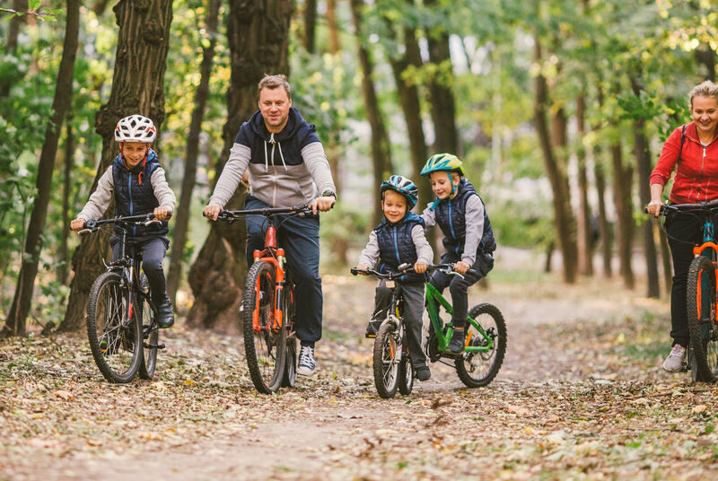 Two parents and their three children wearing protective helmets riding their bikes on a path in the woods.