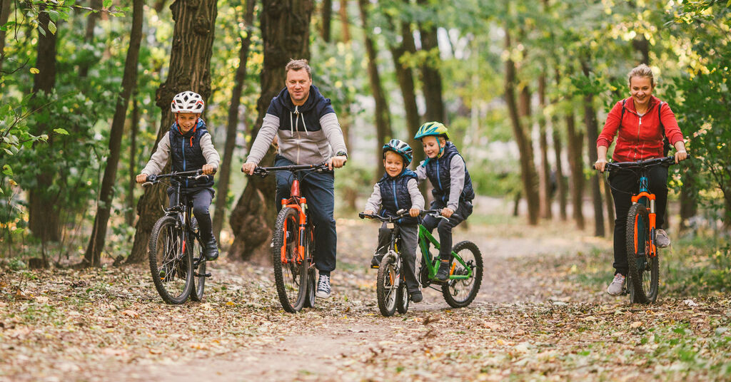 Two parents and their three children wearing protective helmets riding their bikes on a path in the woods.